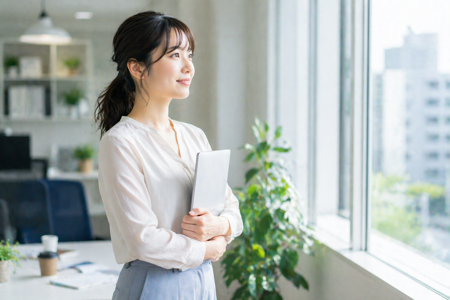 明るいオフィスの窓際でタブレットを抱えながら前向きな表情を見せる20代女性が、自分に合う事務職や理想の働き方を考えている様子を表現したコラム用画像